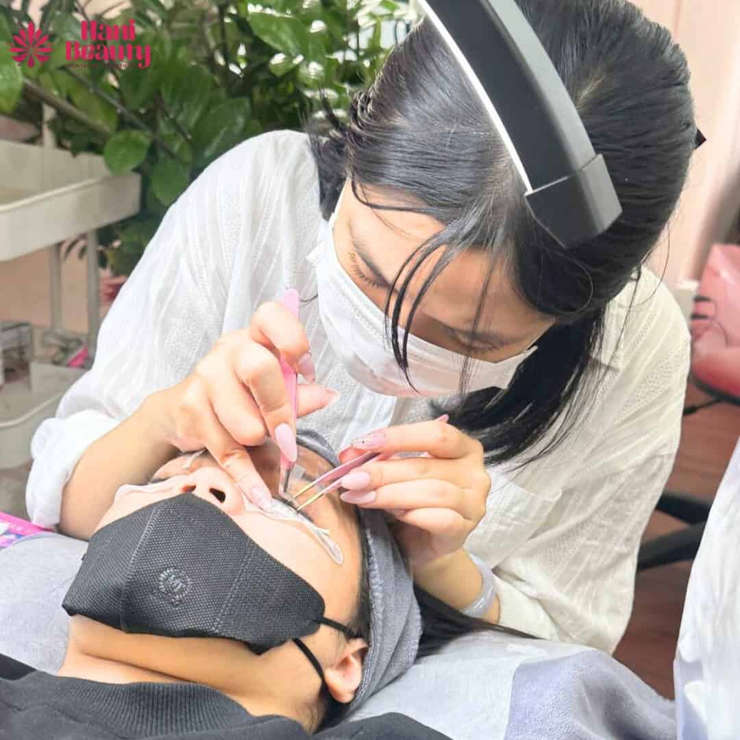 Thợ nối mi đang thao tác với khách, không khí thoải mái và nhẹ nhàng.