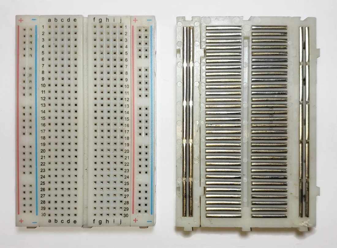 Ảnh chụp một breadboard nhỏ: bên trái mặt trước có hàng lỗ đánh số 1 đến 30, cột a đến j, hai dải nguồn đỏ xanh hai bên; bên phải mặt sau đã bóc lớp đế, thấy các thanh kim loại nằm ngang nối từng hàng năm lỗ và các thanh dài dọc theo dải nguồn