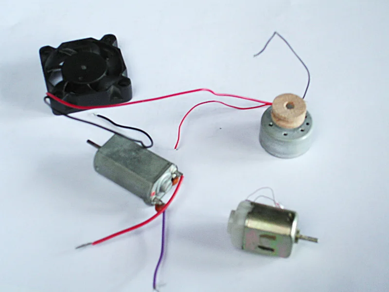 Ảnh chụp các motor DC nhỏ có chổi than vỏ kim loại hai dây đỏ, cỡ gần với motor 140 mini, nằm cạnh một quạt tản nhiệt nhỏ