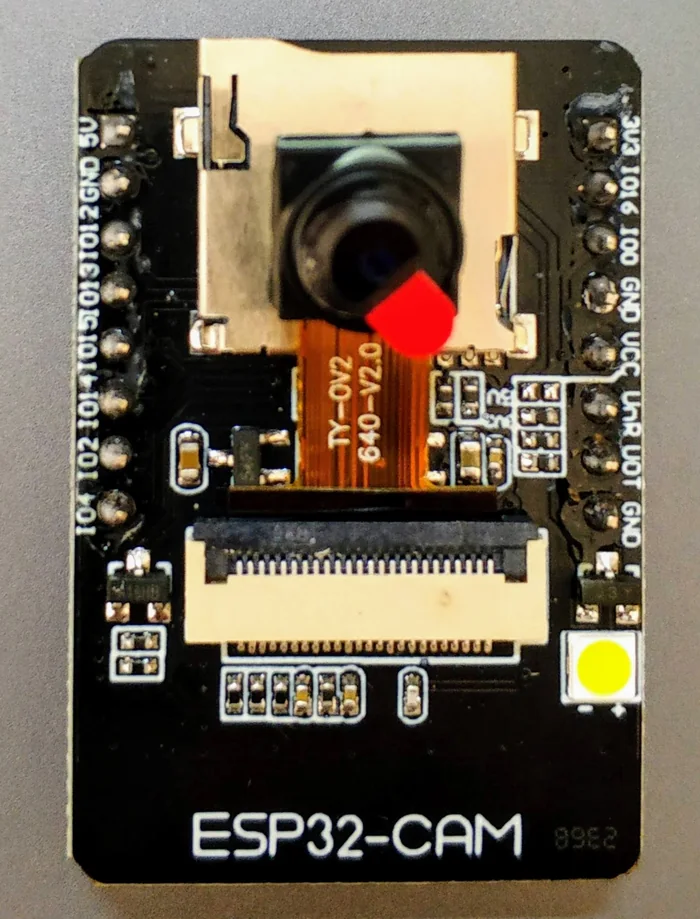 Module ESP32-CAM màu đen với camera OV2640, khe thẻ nhớ microSD, đèn LED trắng và hai hàng chân có chân 5V, GND ở góc trên bên trái