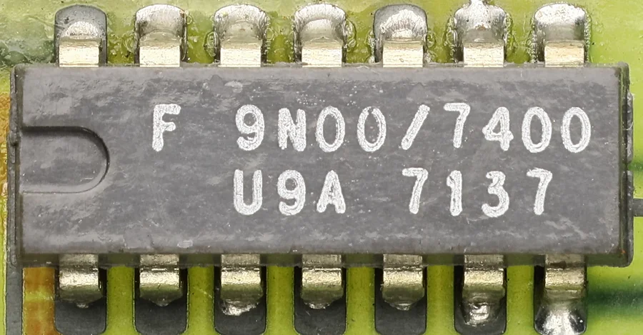 Ảnh chụp cận cảnh IC 7400 vỏ DIP 14 chân màu xám đen hàn trên mạch in màu xanh vàng, trên thân in chữ F 9N00/7400 và dòng U9A 7137, khấc đánh dấu ở đầu bên trái