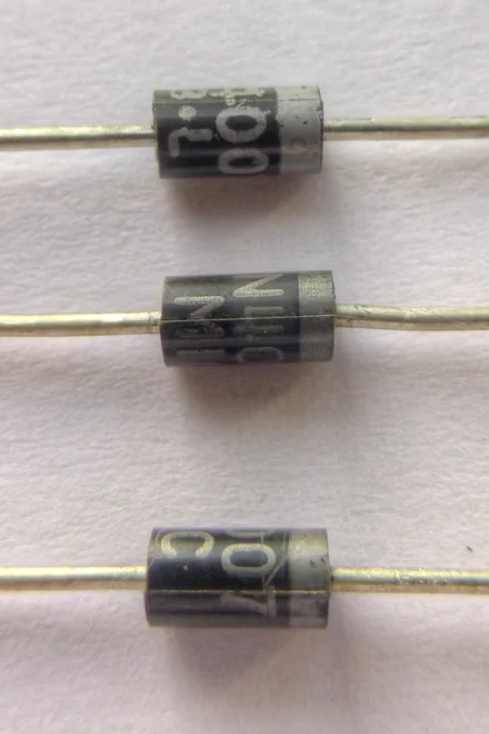 Ảnh chụp ba diode chỉnh lưu 1N4007 thân nhựa đen hình trụ, chân dài hai đầu, mỗi diode có vạch màu xám ở một đầu đánh dấu cathode và chữ in mã diode