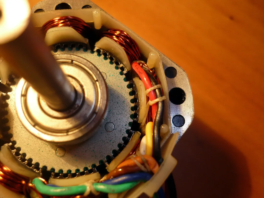 Bên trong động cơ bước lai đã tháo nắp: trục giữa, rotor có nhiều răng nhỏ, các cuộn dây đồng quấn trên răng stator và dây ra nhiều màu