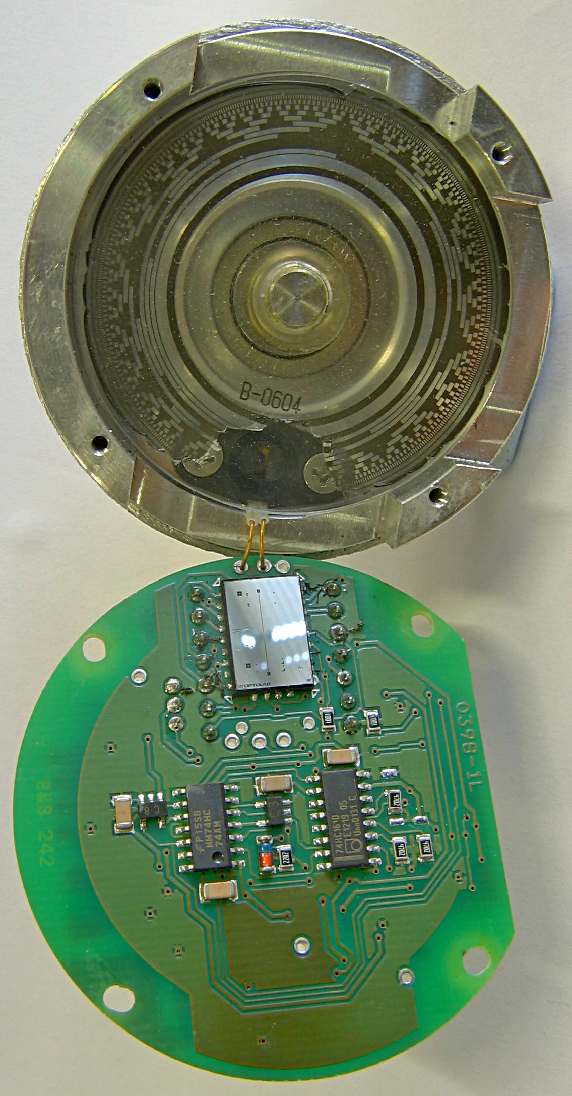 Encoder tuyệt đối mã Gray 13 vòng được mở ra: phía trên là vỏ nhôm với đĩa thủy tinh có các vòng vạch đồng tâm, phía dưới là mạch in có chip cảm biến quang phản xạ và các IC xử lý