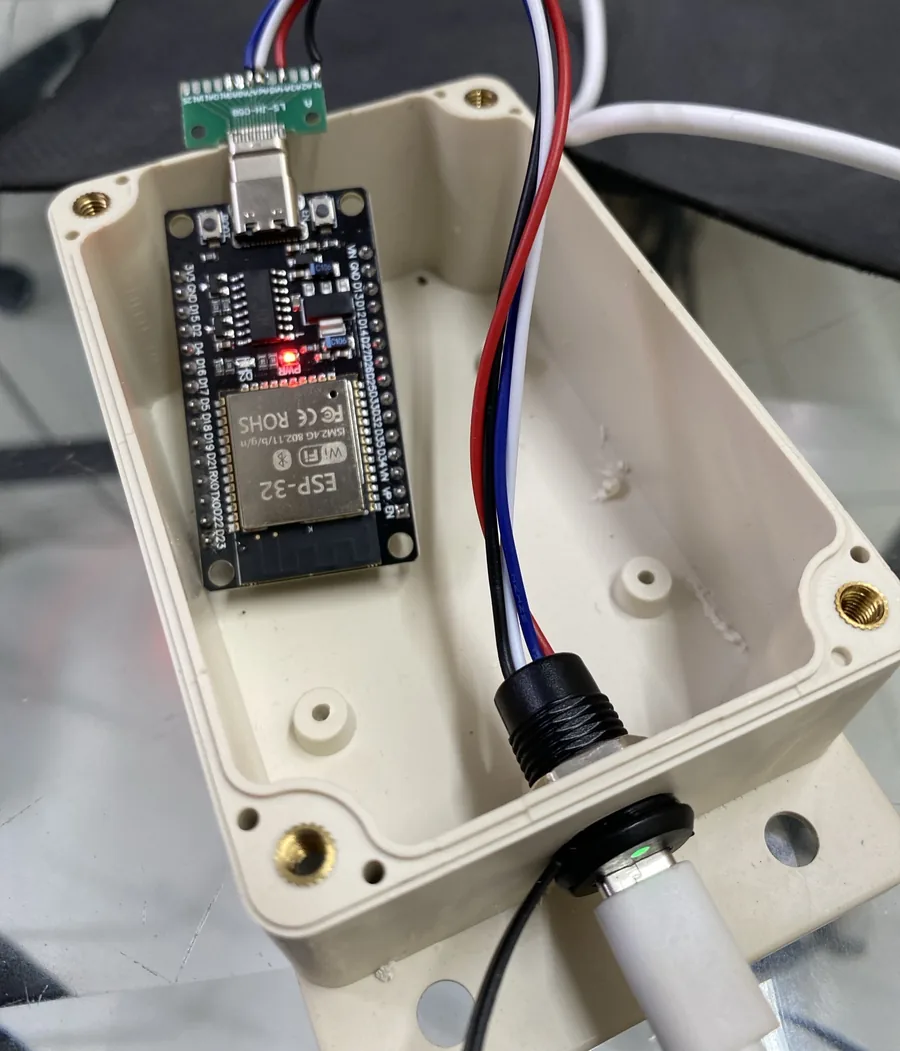 Bo ESP32 DevKit đặt trong hộp nhựa, đầu Type-C đực cắm vào cổng của bo, bốn dây đỏ, đen, trắng, xanh dương đi dọc vách hộp tới jack Type-C