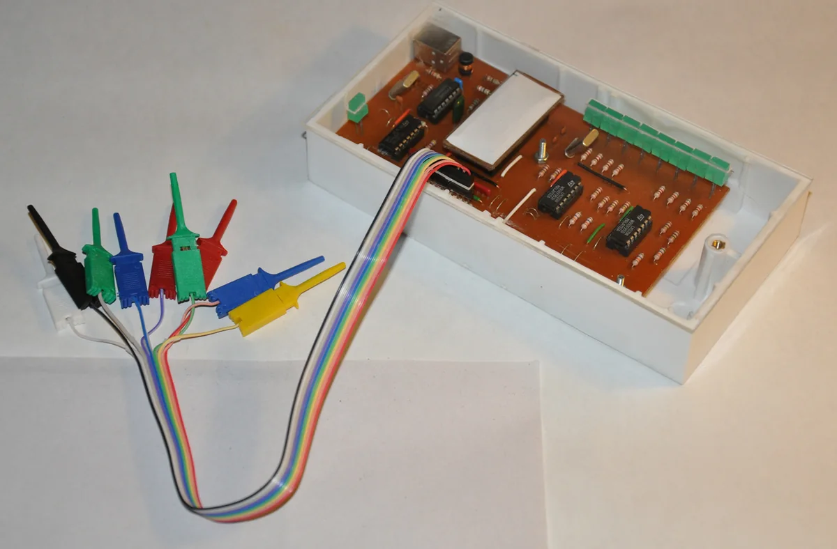 Một logic analyzer 8 kênh tự làm: mạch in trong hộp nhựa trắng, cổng USB, dải LED báo mức, dây cáp dẹt nhiều màu nối tới các kẹp móc đo