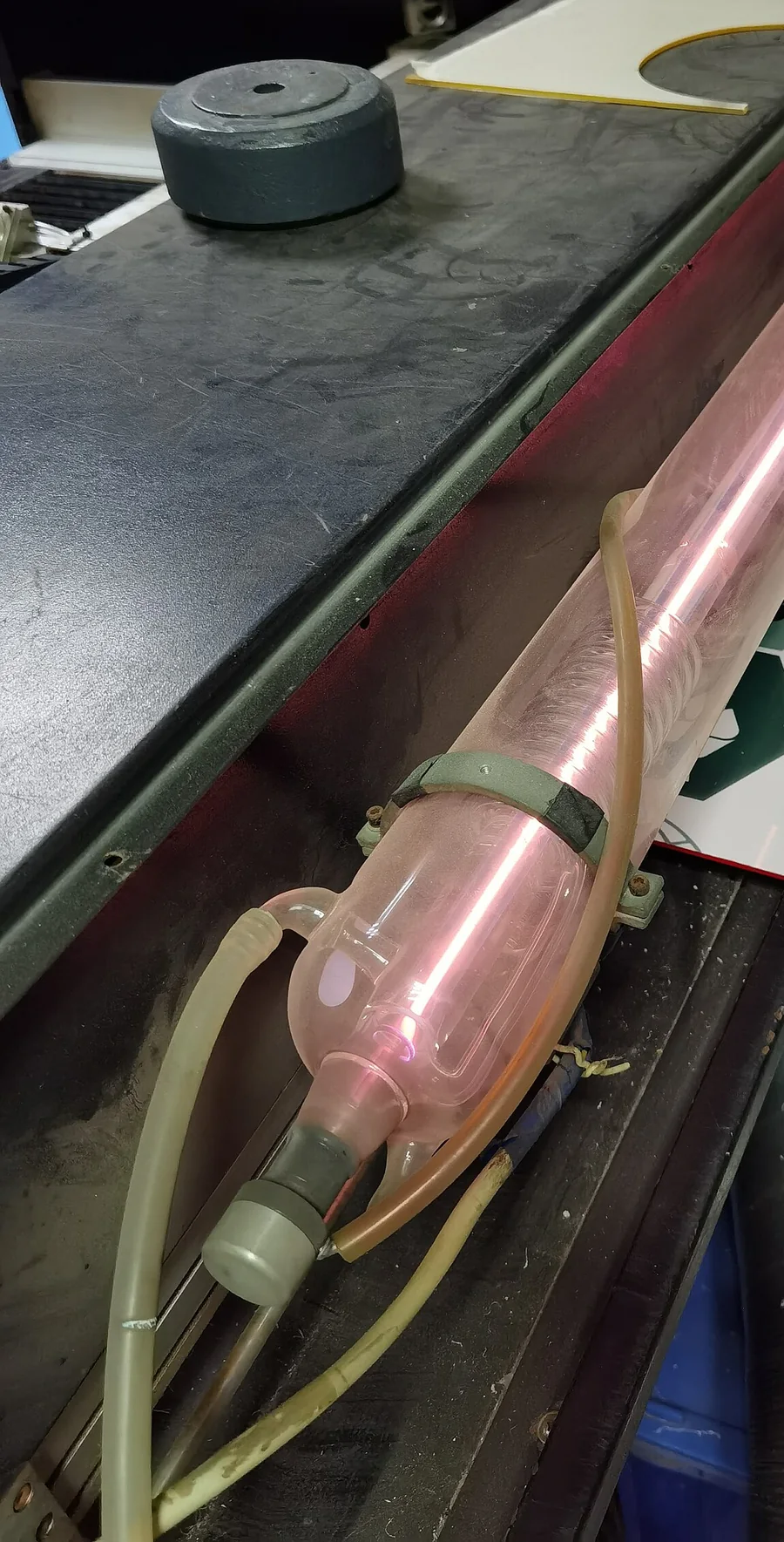 Ống laser CO2 bằng thủy tinh màu hồng nhạt nằm trong thân máy cắt, có ống nước làm mát luồn quanh hai đầu ống