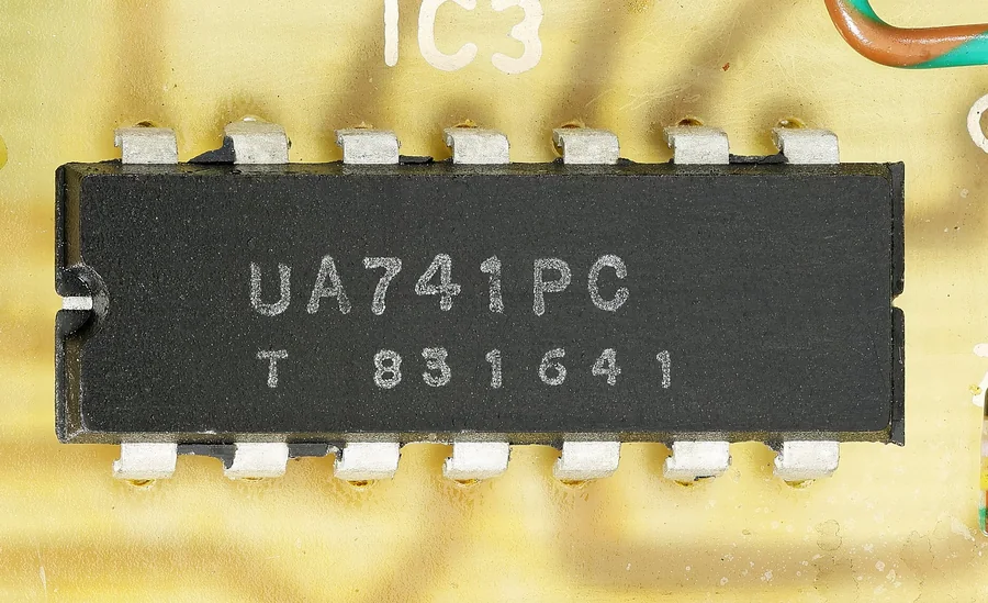 Ảnh chụp cận cảnh một IC op-amp µA741 vỏ DIP 14 chân màu đen hàn trên mạch in màu vàng nhạt, trên thân in chữ UA741PC và dòng số, khấc đánh dấu ở đầu bên trái, chữ IC3 in trên mạch phía trên