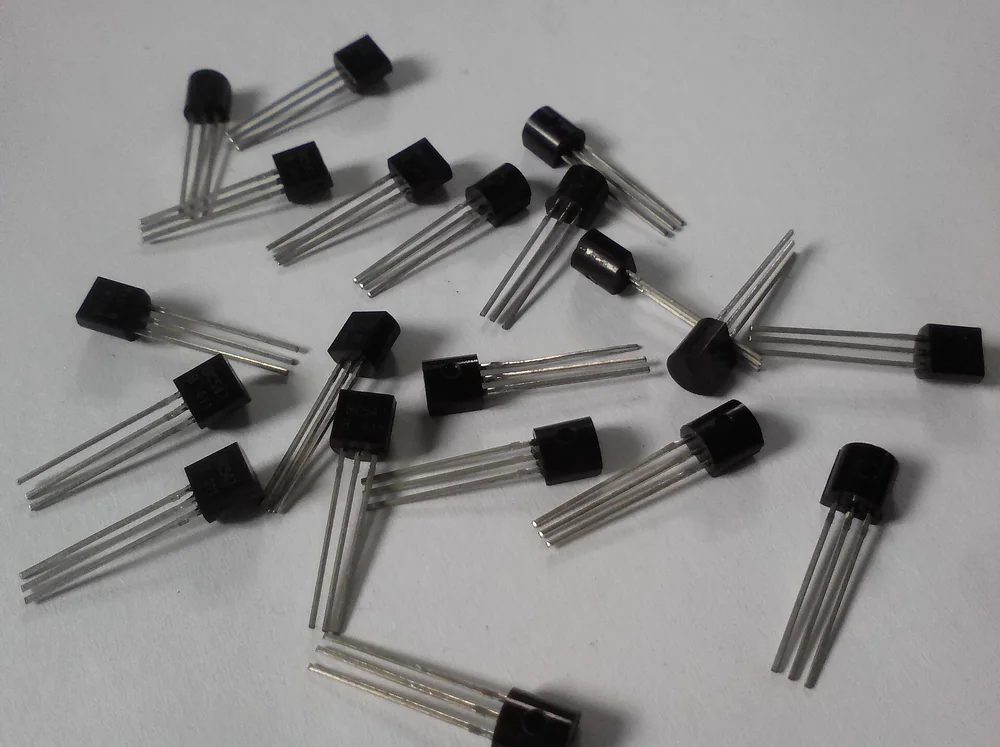 Ảnh chụp nhiều transistor nhỏ vỏ nhựa đen TO-92 hình bán nguyệt, mỗi con ba chân, nằm rải trên nền trắng