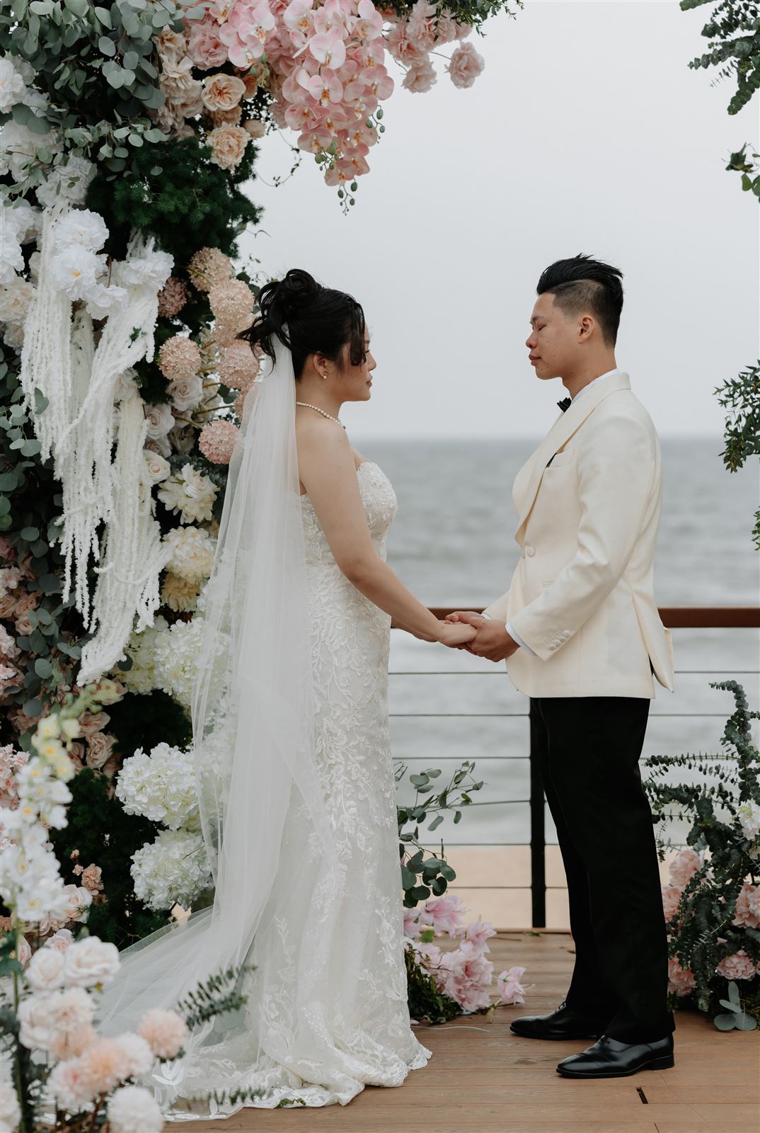 Thuỷ Tiên và Tuấn Vũ nắm tay dưới cổng hoa bên biển tại Mikazuki Resort Đà Nẵng