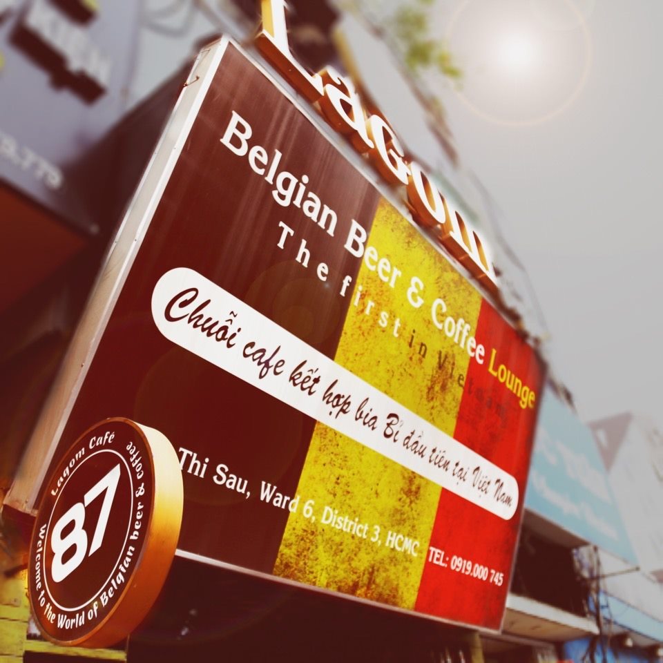 Bảng hiệu Lagom Café nổi bật với dòng chữ “Chuỗi café kết hợp bia Bỉ đầu tiên tại Việt Nam”, trên nền lá cờ Bỉ đặc trưng ba màu đen-vàng-đỏ Bảng hiệu Lagom Café nổi bật với dòng chữ “Chuỗi café kết hợp bia Bỉ đầu tiên tại Việt Nam”, trên nền lá cờ Bỉ đặc trưng ba màu đen-vàng-đỏ